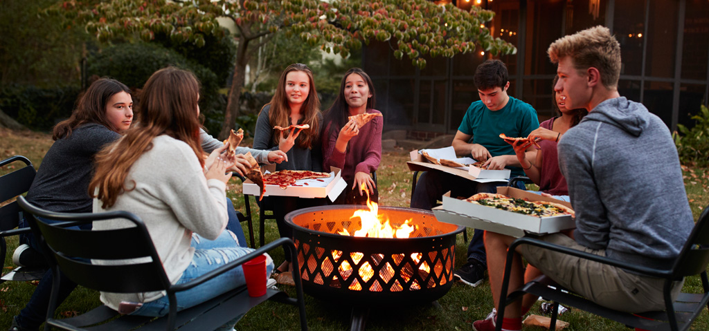 teenage-friends-sit-round-fire-pit-eating-takeaway-pizza